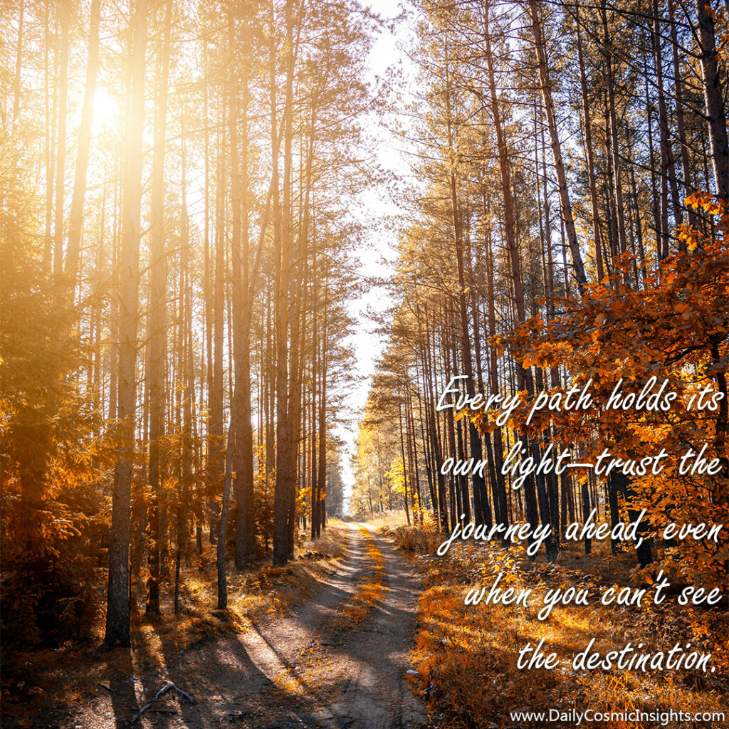 A dirt road leads through an autumn colored woods, sunlight streaming through the branches and leaves above. The text reads, "Every path holds its own light—trust the journey ahead, even when you can't see the destination."